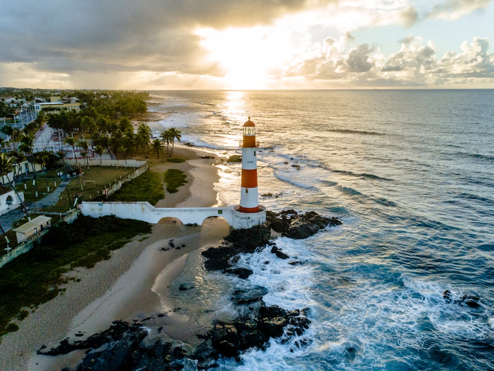 white and orange lighthouse beside sea