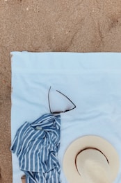 A sunny outdoor scene featuring a straw sunhat with a wide brim on a beach towel.