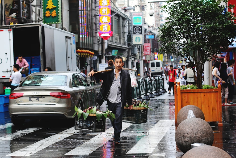 vendor man carrying two baskets hang on stick crossing road