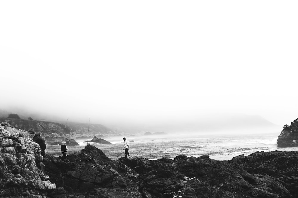 gray scale photo of man standing on rock shore