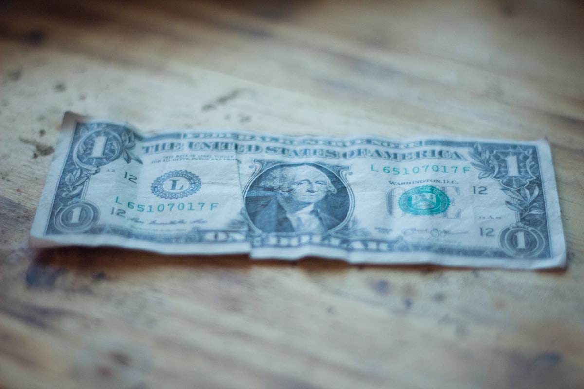 A single U.S. dollar bill resting on a worn wooden desk.