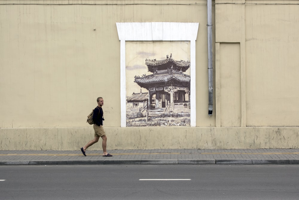 minimalist photography of man walking along pagoda wall artwork