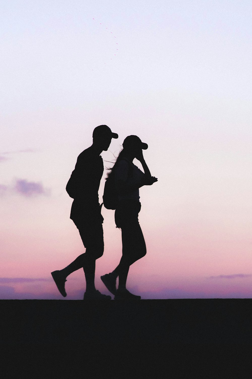 silhouette photo of man and woman wearing caps