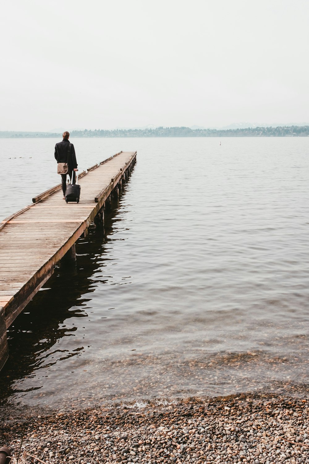 person walking on dock while towing luggage bag