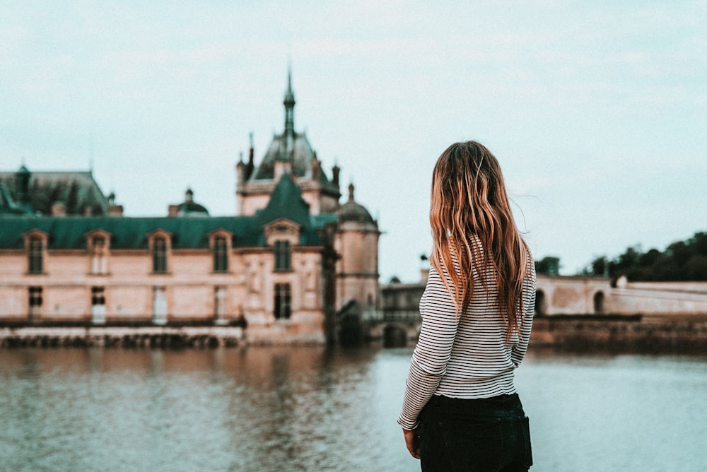 Femme face à un bâtiment en béton beige et vert et à un plan d’eau