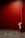 A red fire extinguisher is mounted against a red-walled corner. The floor is covered with black and gray tiles, and there's a small sign attached to the extinguisher.