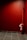 A red fire extinguisher is mounted against a red-walled corner. The floor is covered with black and gray tiles, and there's a small sign attached to the extinguisher.