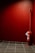 A red fire extinguisher is mounted against a red-walled corner. The floor is covered with black and gray tiles, and there's a small sign attached to the extinguisher.