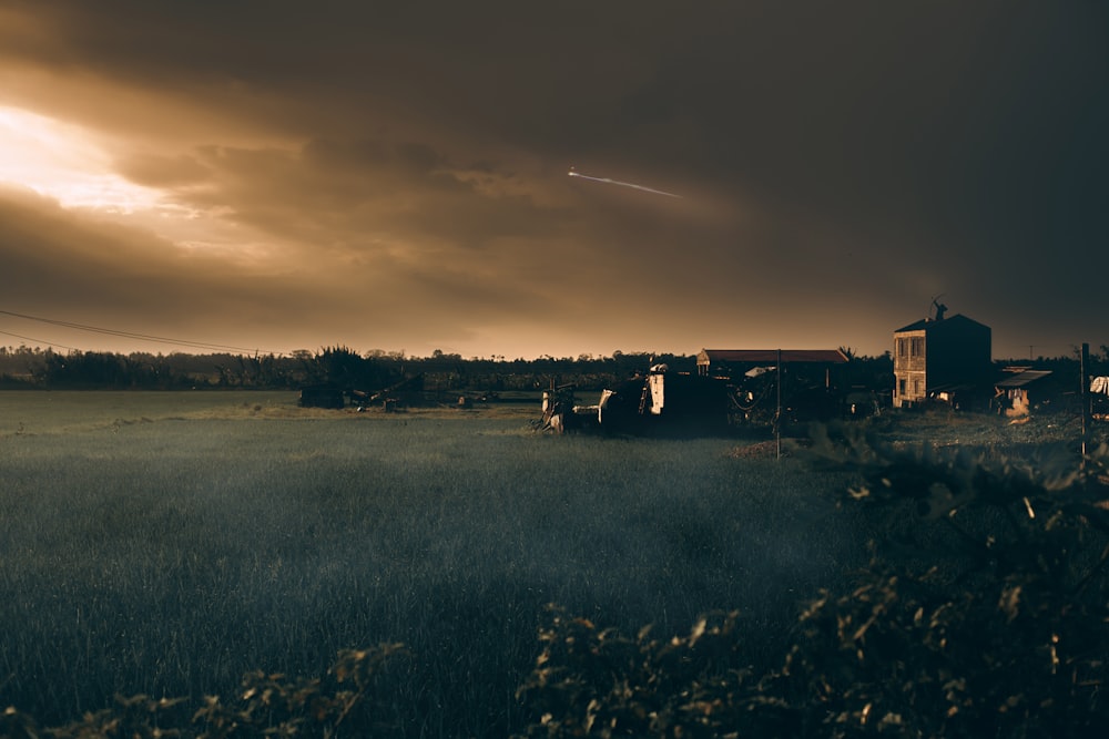 a field with a house and a plane in the sky