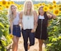 three women standing between sunflowers