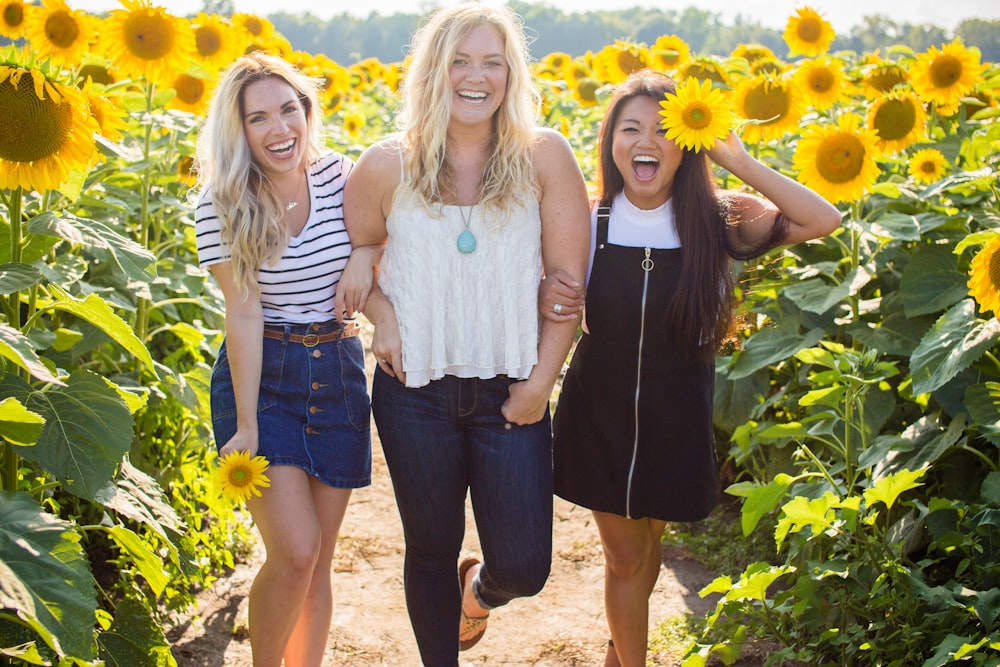three women standing between sunflowers
