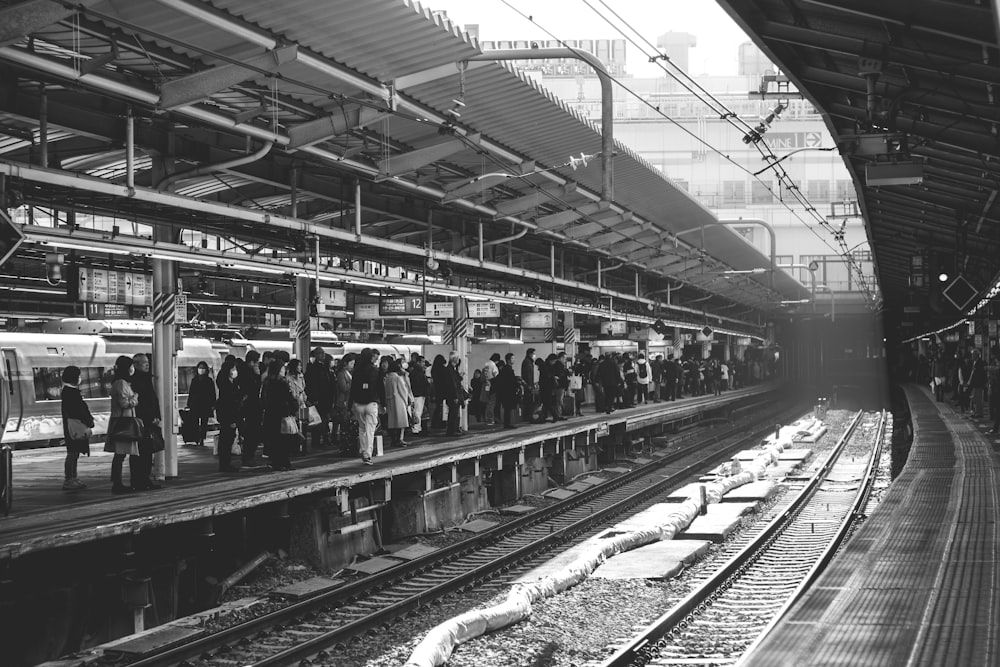 Foto en escala de grises de un grupo de personas que caminan en la estación de tren