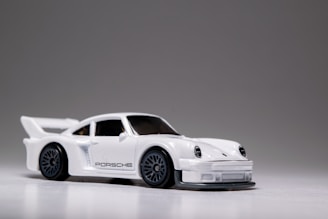 A small, detailed model car with a sleek white finish and prominent black detailing. The car features a spoiler, black wheels, and intricate headlight designs.