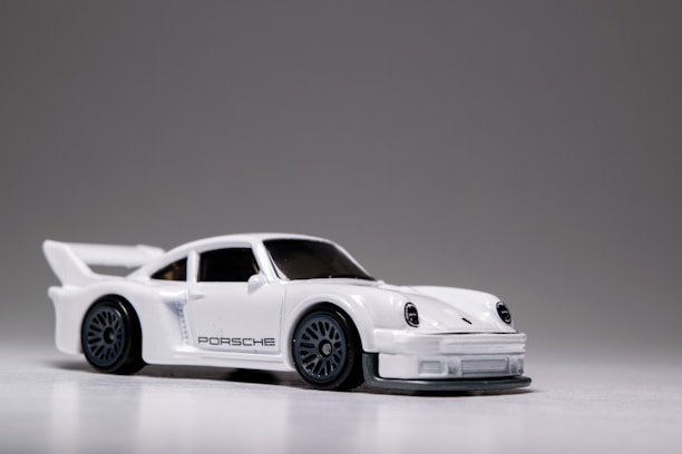A small, detailed model car with a sleek white finish and prominent black detailing. The car features a spoiler, black wheels, and intricate headlight designs.