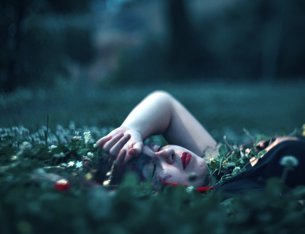 woman closing eyes lying on green grass