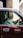 A man sits in the driver’s seat of a classic taxi, wearing a formal white shirt. Sunlight streams through the window, casting reflections on the vehicle's maroon exterior. The taxi sign on the car door includes Japanese script along with the word 'taxi'.