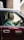 A man sits in the driver’s seat of a classic taxi, wearing a formal white shirt. Sunlight streams through the window, casting reflections on the vehicle's maroon exterior. The taxi sign on the car door includes Japanese script along with the word 'taxi'.