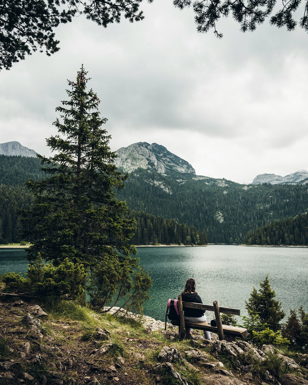 woman sitting on bench facing lake