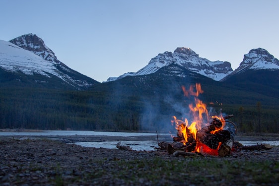 A cozy campfire scene surrounded by mountains with a person wearing a nature-themed motivational shirt.