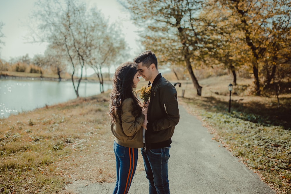 man and woman facing each other standing on footpath beside body of water