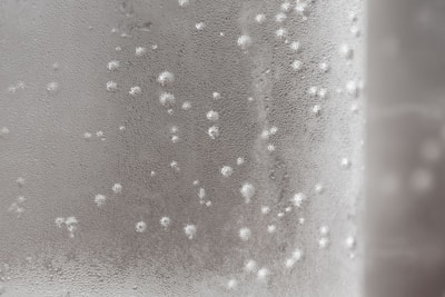 Condensation covers a transparent or semi-transparent surface, forming small droplets across the area. The glass or material appears misty, with varying sizes of water beads scattered throughout.