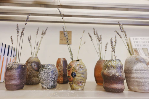 A collection of small ceramic vases in cheerful pastel shades arranged on a rustic shelf.