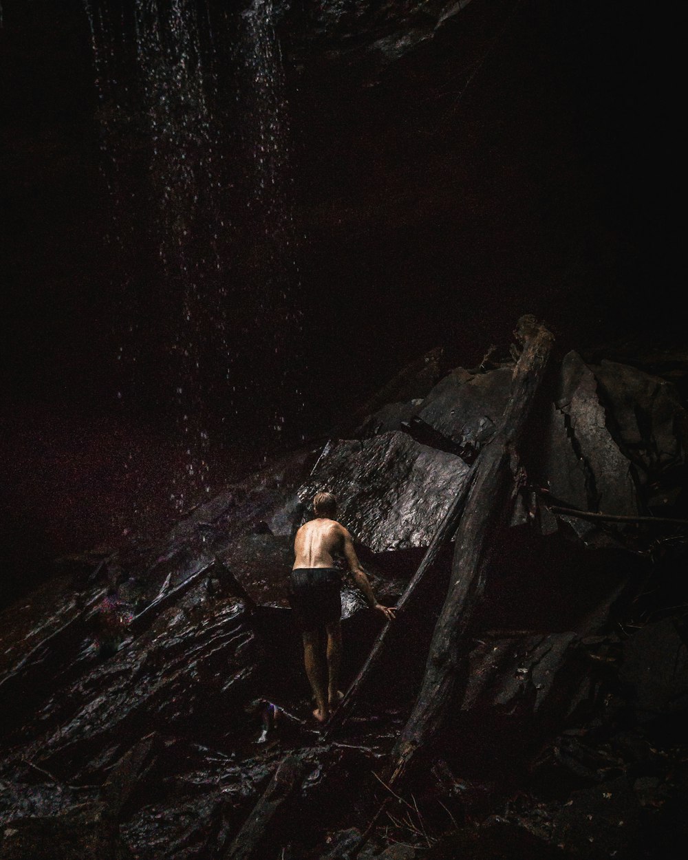 topless man standing at the bottom of waterfall