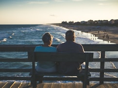 man and woman sitting on bench in front of beach