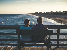 man and woman sitting on bench in front of beach