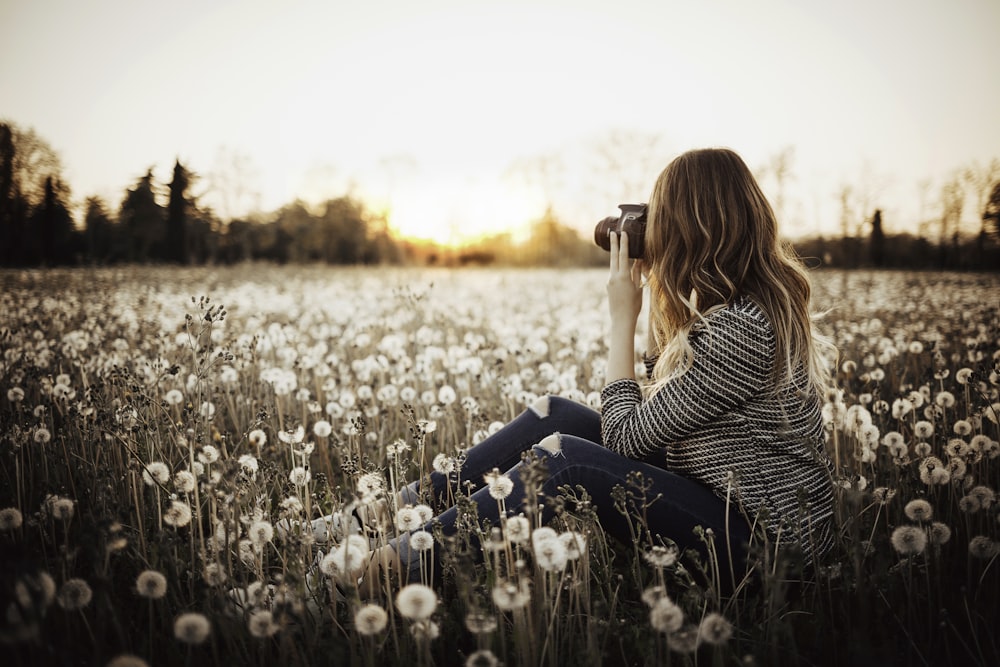 花畑に座って木の写真を撮る女性