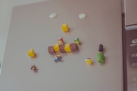 A collection of small, colorful Super Mario-themed magnets is attached to a refrigerator surface. These include Mario, question blocks, mushrooms, and a green pipe, resembling elements from the iconic video game series.