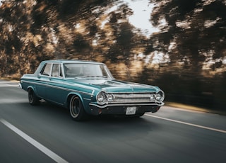 teal sedan on roadway beside the trees