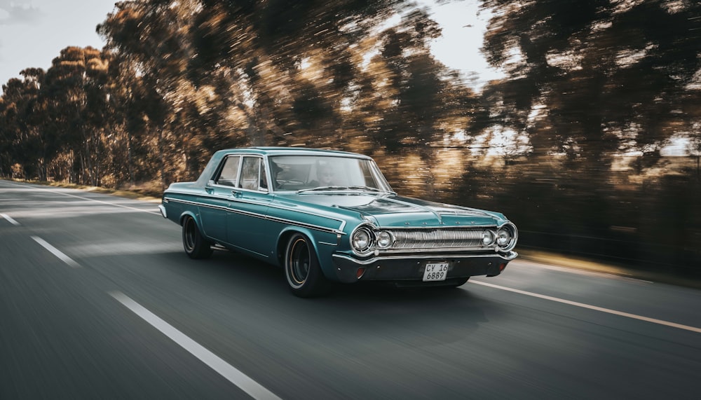 teal sedan on roadway beside the trees