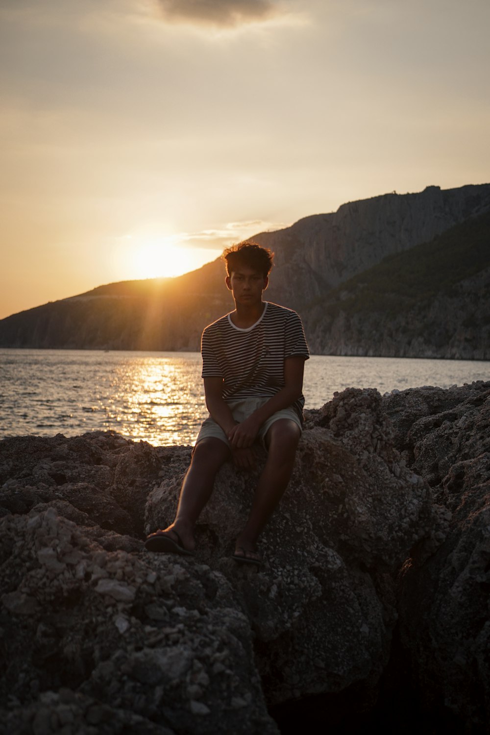 uomo che si siede sulla roccia vicino al mare all'ora d'oro