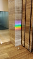 A polished marble wall and floor create a sleek and modern interior scene. A vibrant rainbow reflection appears on the marble surface, originating from an unseen light source. The colors of the rainbow stand out against the neutral tones of the marble.