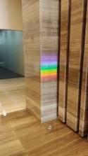 A polished marble wall and floor create a sleek and modern interior scene. A vibrant rainbow reflection appears on the marble surface, originating from an unseen light source. The colors of the rainbow stand out against the neutral tones of the marble.