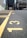A close-up view of a paved parking lot with yellow painted lines and numbers on the ground. The numbers 13, 14, and 15 are clearly visible. In the background, there are buildings and cars, but they are out of focus.