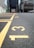 A close-up view of a paved parking lot with yellow painted lines and numbers on the ground. The numbers 13, 14, and 15 are clearly visible. In the background, there are buildings and cars, but they are out of focus.
