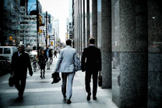 people walking on sidewalk pathway beside road with vehicles and high-rise buildings during daytime