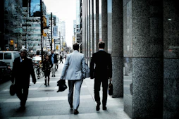people walking on sidewalk pathway beside road with vehicles and high-rise buildings during daytime