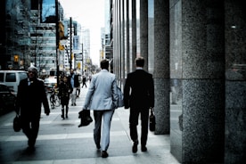 people walking on sidewalk pathway beside road with vehicles and high-rise buildings during daytime