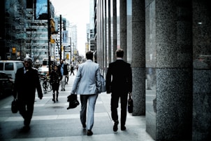 people walking on sidewalk pathway beside road with vehicles and high-rise buildings during daytime