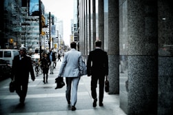 people walking on sidewalk pathway beside road with vehicles and high-rise buildings during daytime