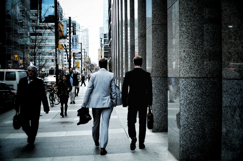 people walking on sidewalk pathway beside road with vehicles and high-rise buildings during daytime