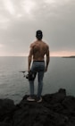 back view of topless man standing on cliff while holding camera