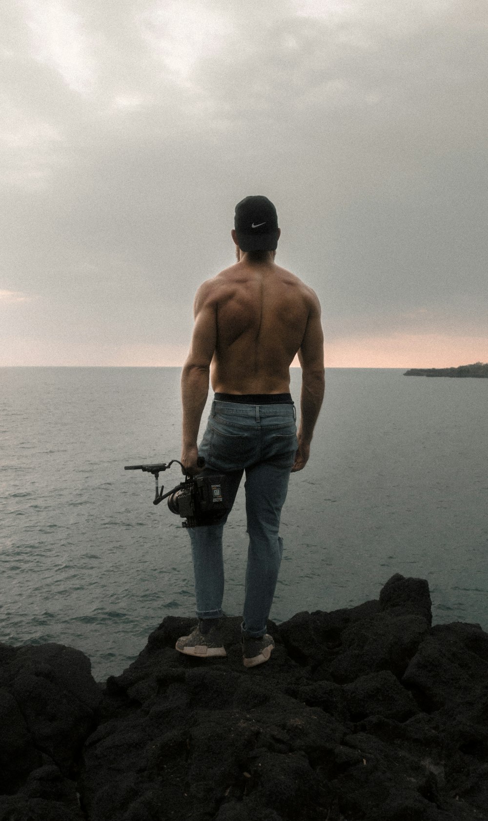 back view of topless man standing on cliff while holding camera