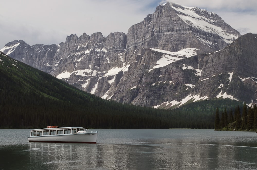 white cruise ship on body of water near rocky mountain