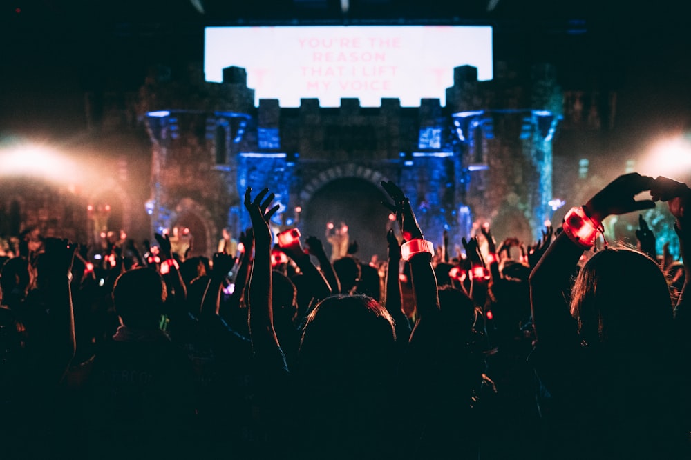 pessoas aglomeradas usando pulseira de LED levantando as mãos em frente ao palco