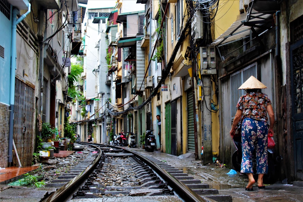 person walking on railway side between buildings at daytime