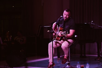 Rob Faler performing an intimate set in a smoky nightclub with acoustic guitar.